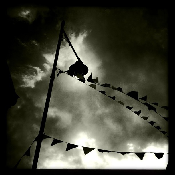 Silhouette of a person on a rope swing against a dramatic cloudy sky, with bunting strung across.