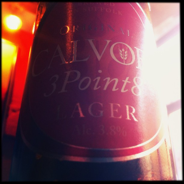 A bottle of lager beer backlit by warm neon lighting, with a red glow illuminating the label and creating a hazy effect.