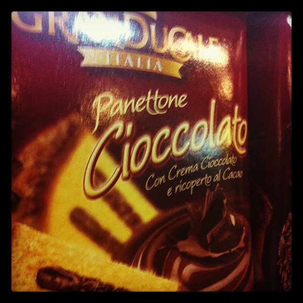 A Panettone Cioccolato box is displayed, showing chocolate cake packaging with Italian text and cocoa imagery against a warm-lit background.