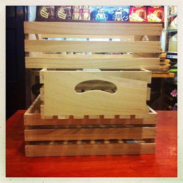 Stacked wooden crates with slatted sides on a red surface, displayed indoors with shelving and boxes visible in the background.