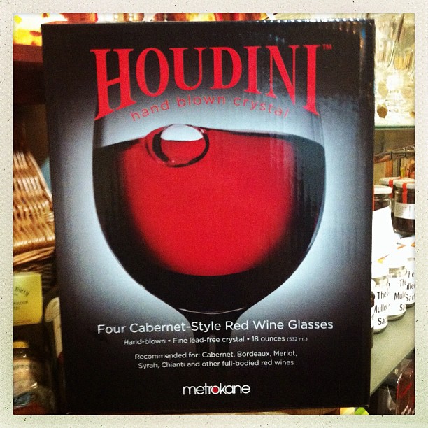 Houdini hand-blown crystal wine glasses packaging showing a red wine glass against a dark background in a shop.