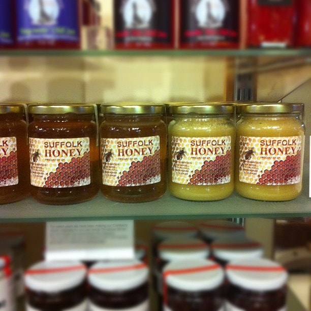 Five jars of Suffolk Honey displayed on a shelf, with darker honey on the left transitioning to lighter honey on the right.