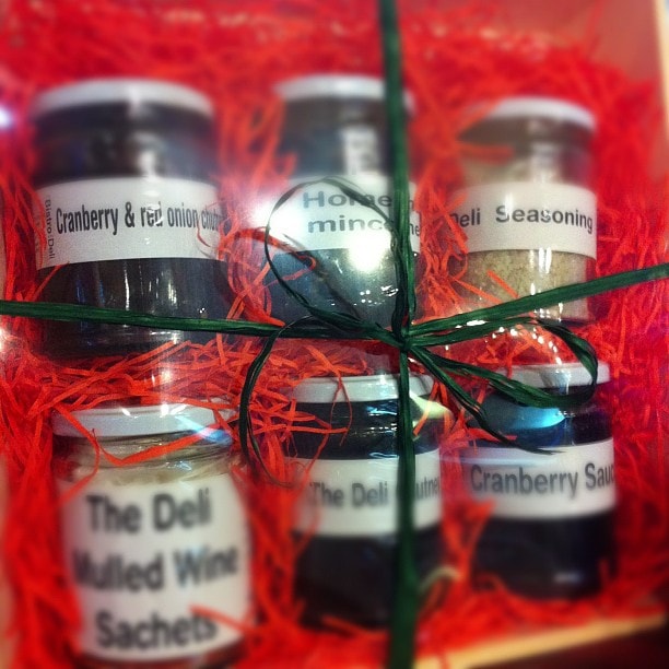 A gift set of four small bottles with labels, tied together with green twine on red crinkle paper packaging.