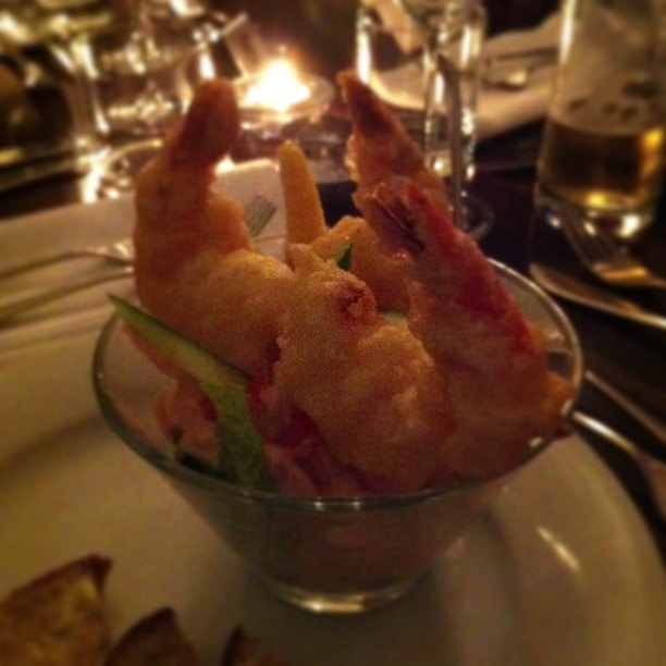 Fried prawn appetisers served in a glass bowl at an upmarket restaurant table with candlelight in the background.