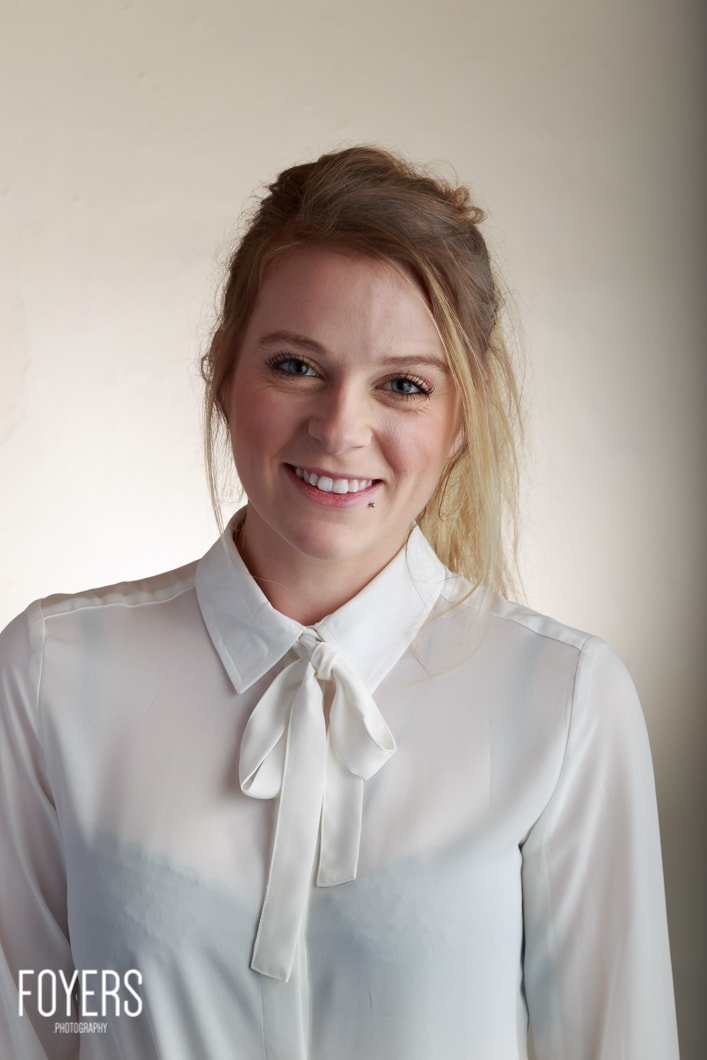 Woman smiling in white blouse with bow.