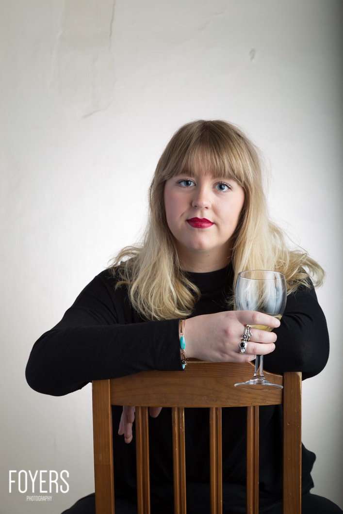 Woman with a glass of wine, sitting on chair.