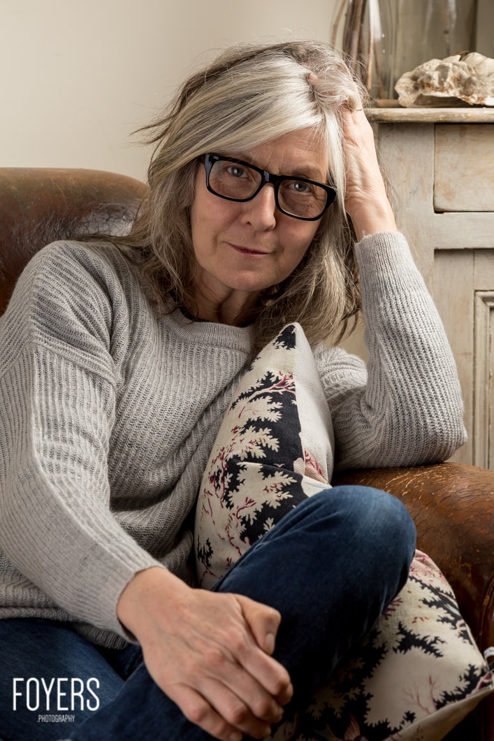Woman in glasses sitting with cushion on chair.