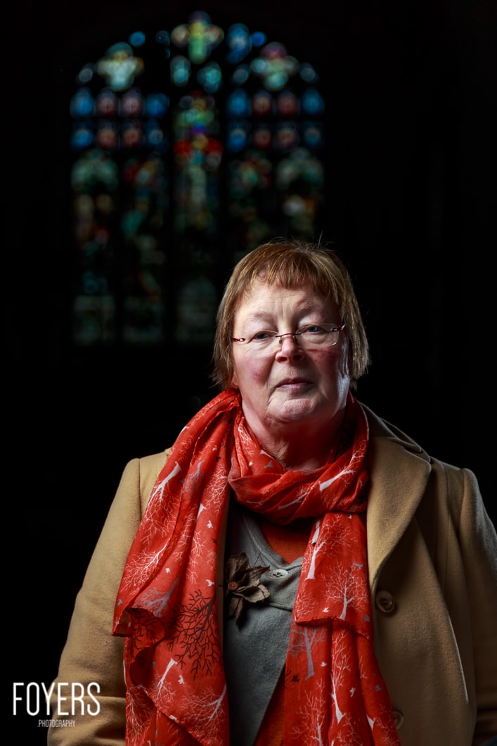 Woman in red scarf by stained glass window.