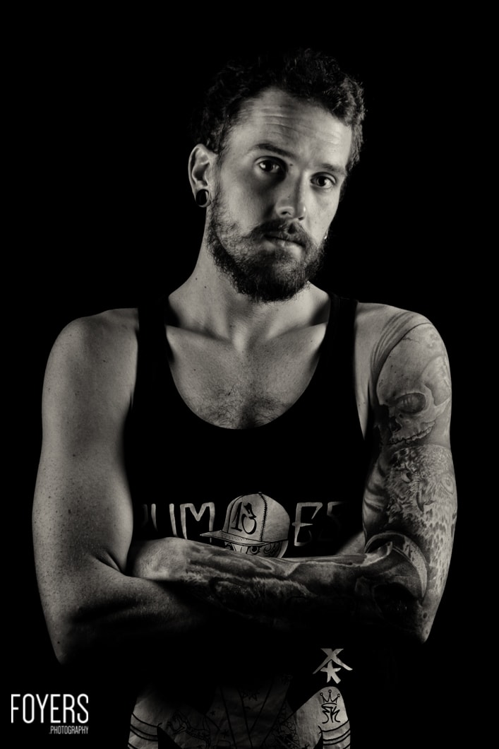 Tattooed man in sleeveless shirt, monochrome portrait.