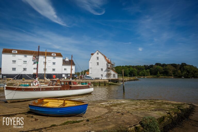 Boats moored near historical white building on riverbank.