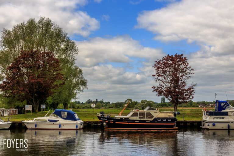 Boats moored on a canal under cloudy sky.