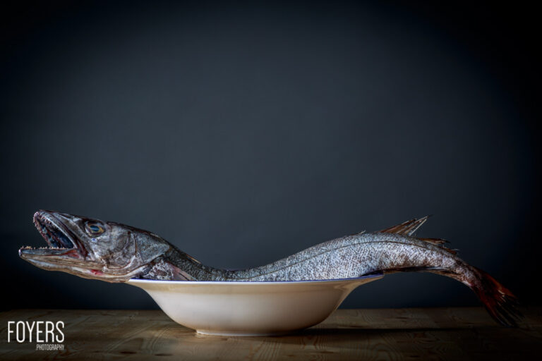 Whole fish in a bowl on wooden table.