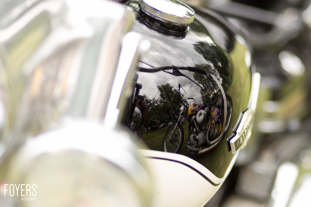 Chrome motorcycle fuel tank with reflection of custom bike with flame design and trees in polished surface