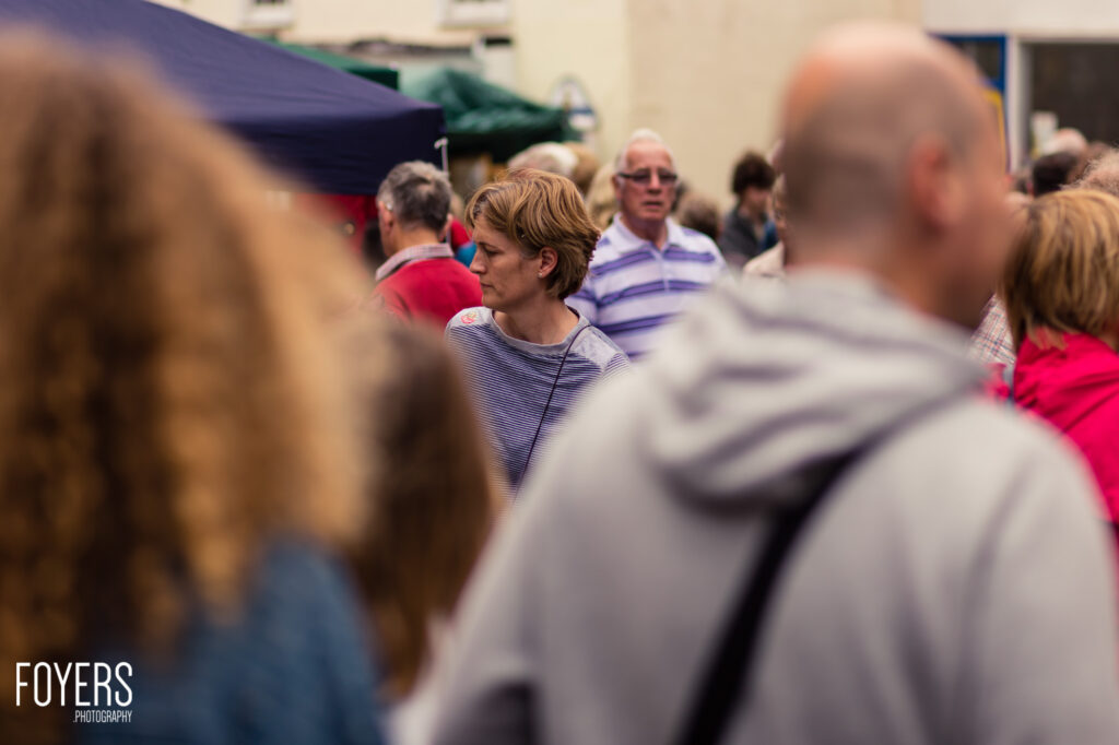 A woman in a striped top stands in the middle of a crowded outdoor area, surrounded by blurred people in the foreground and background.