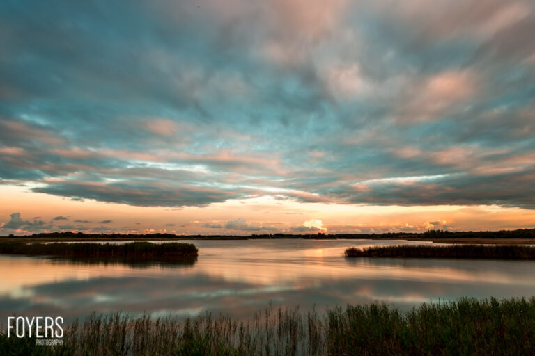 Sunset over reed beds and the River Alde at Snape, Suffolk, with teal and orange clouds reflected in the water