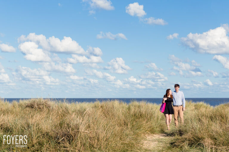 Young couple walking hand in hand through dunes and marram grass on the Suffolk coast, sea in the background