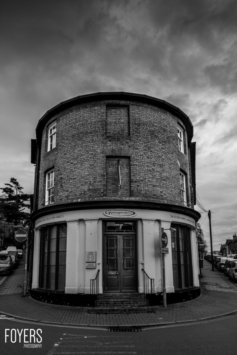 A cylindrical brick building with a curved white storefront at street level, housing Gyrophobics business, under cloudy sky.