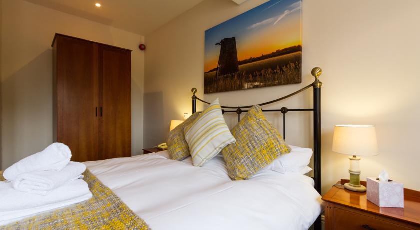 A neatly made double bed with white sheets and yellow patterned cushions in a modern bedroom with warm lighting.