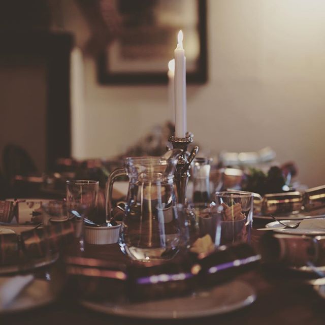 A lit white candle in a crystal candlestick holder on a formal dining table, surrounded by glassware and place settings.