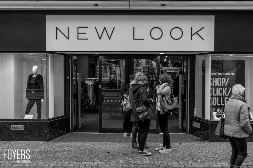 A New Look shop storefront with mannequin in window. Three women stand outside on a paved street, one facing away.