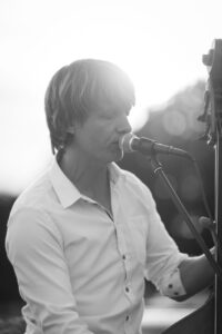 A man in a white shirt singing into a microphone in black and white photography.