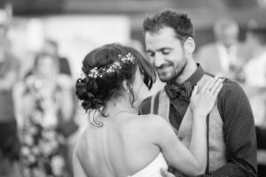 A bride and groom embrace during their wedding ceremony. The bride wears a white dress with flowers in her hair. Black and white photograph.