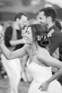 A bride in a white strapless dress with flowers in her hair dances at a wedding reception, smiling broadly.
