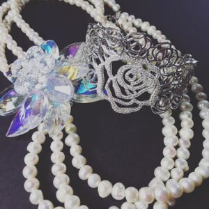 Pearl necklaces with ornate silver pendants featuring crystals and a decorative rose charm on dark background.