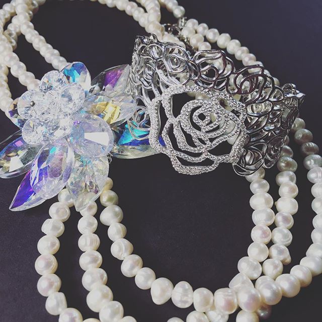 Pearl necklaces with ornate silver pendants featuring crystals and a decorative rose charm on dark background.