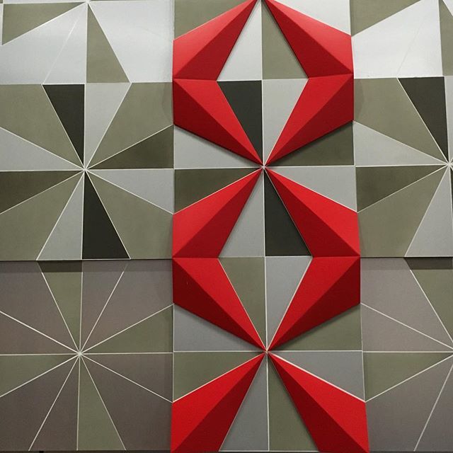 A geometric wall art installation featuring a grid of triangular tiles in beige, grey, and red, creating a three-dimensional star pattern.
