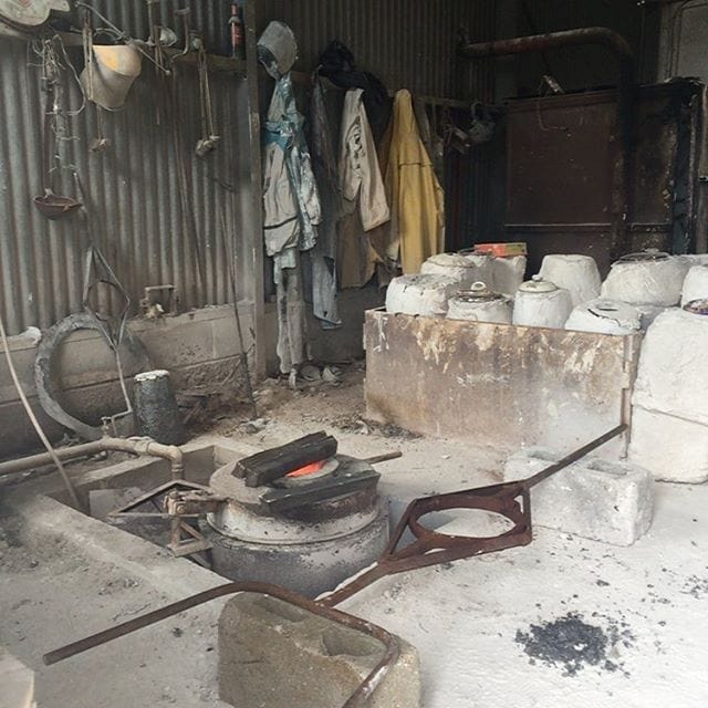 A cluttered workshop or storage shed with cooking equipment, white buckets, hanging clothes, and metal tools scattered on the floor.
