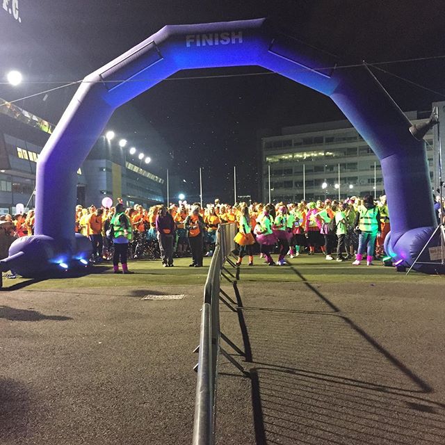 A purple inflatable finish line arch at a nighttime running event with participants in high-visibility clothing gathered around it.