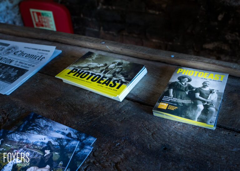 Pamphlets for PhotoFast festival displayed on a weathered wooden table, with yellow and white covers featuring vintage photographs.