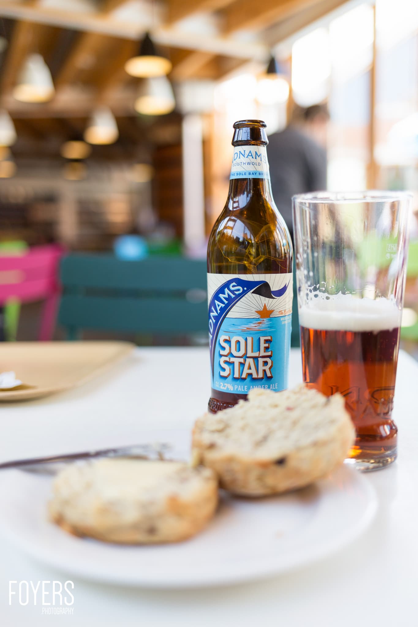 A bottle of Sole Star pale ale sits next to a glass of beer and biscuits on a white plate in a café.
