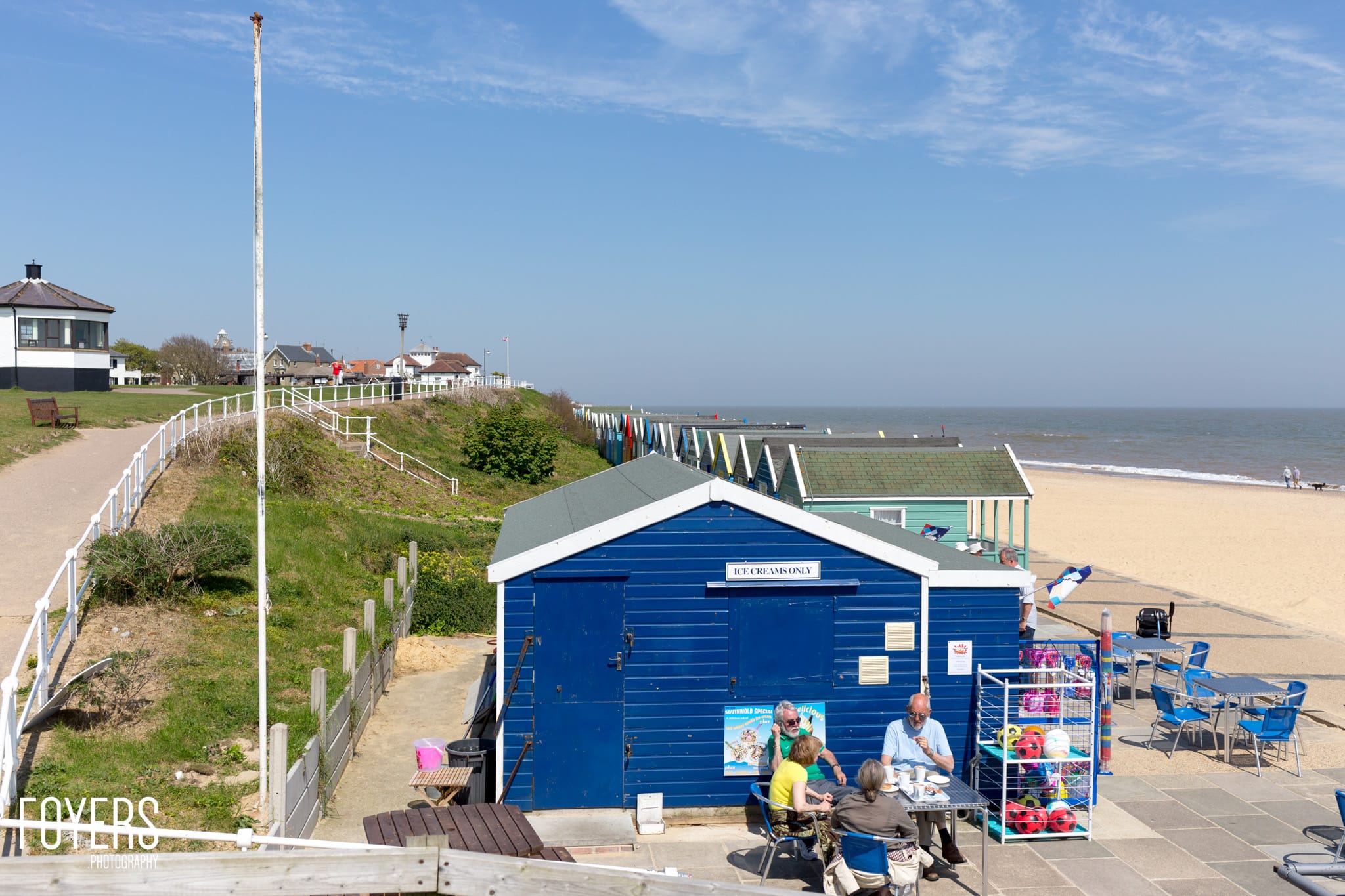 A blue beach hut labeled Ice Creams Only on a sandy beach, with customers being served outside on a sunny day.