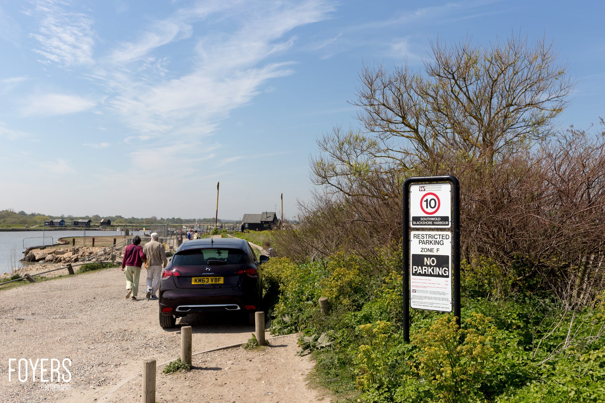 A car parked at Southwold Blackshore Harbour with a no parking sign visible and two people walking nearby.