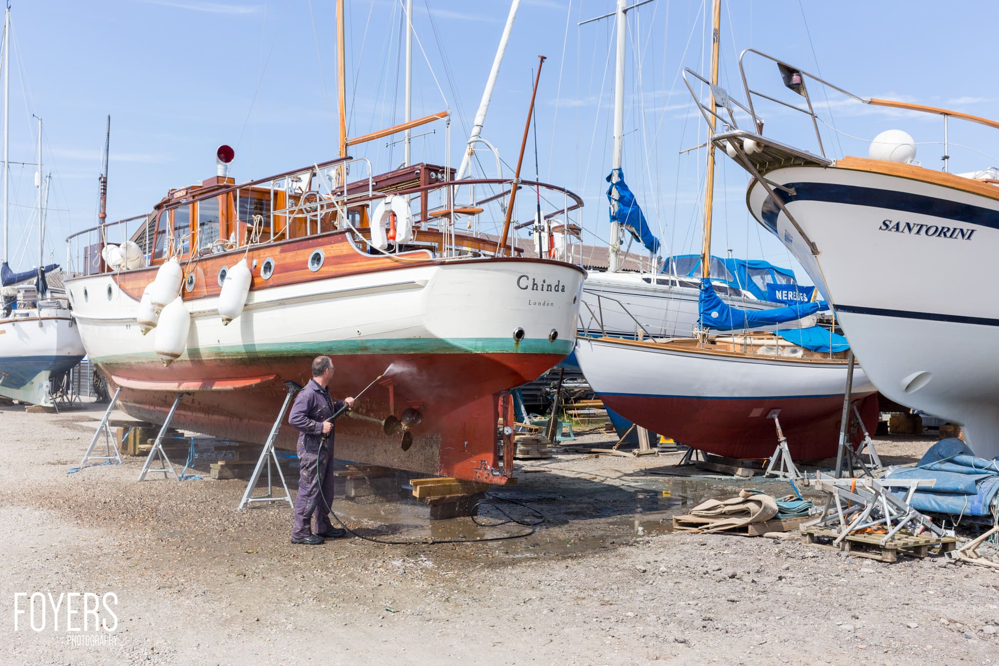 Boats undergoing maintenance on a beach, with a worker spraying the hull of the vessel Chinda in the foreground.