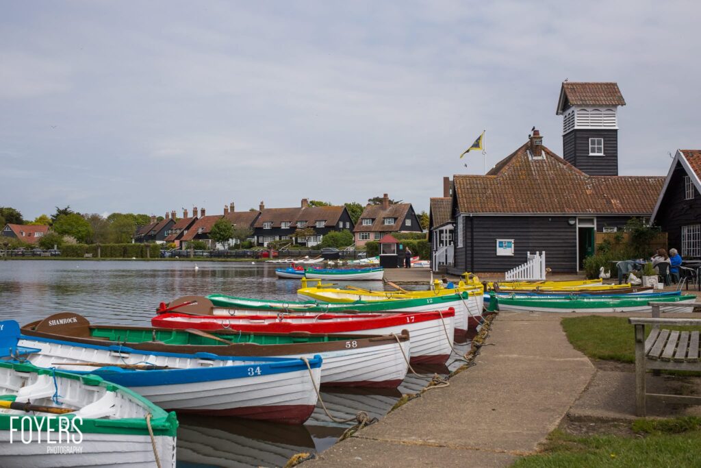 Colourful fishing boats moored along a waterfront with traditional buildings and a boatyard shelter in the background.