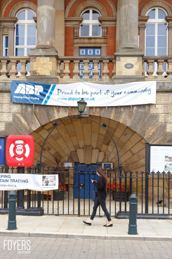 A person walks past a grand Victorian building entrance with a banner reading ABP Proud to be part of your community.