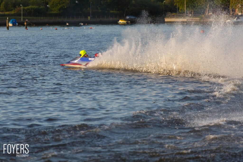 A jet skier in a yellow helmet rides a wave on a blue and yellow jet ski as white spray erupts around them in the sea.