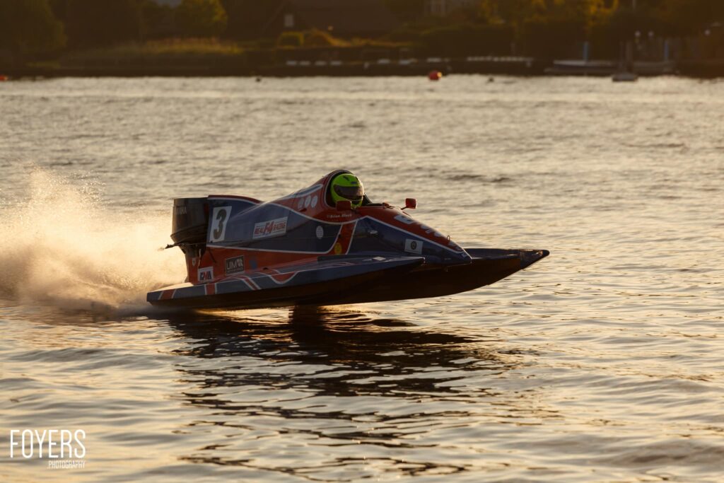 A red and blue speedboat with the number 3 races across water, creating a large spray of water on the left side.