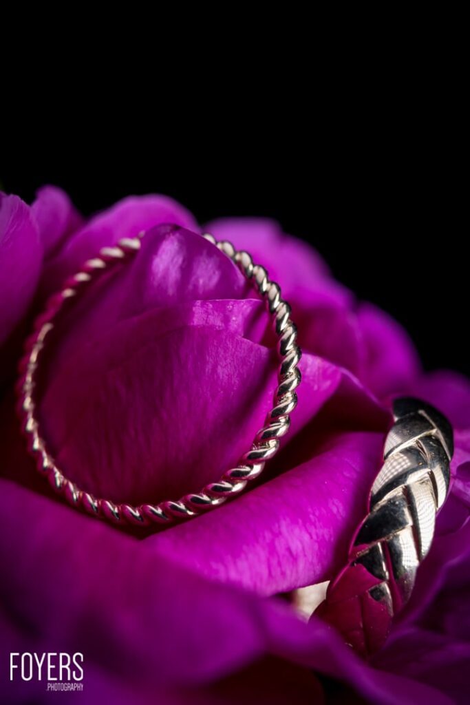 A magenta peony flower with layered petals edged in gold thread, with a bee on its right side, against a black background.