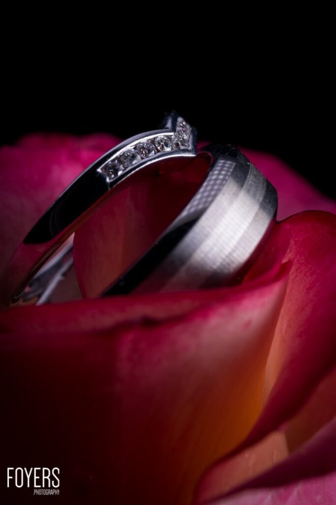 Two wedding rings rest on deep pink and red rose petals against a black background.