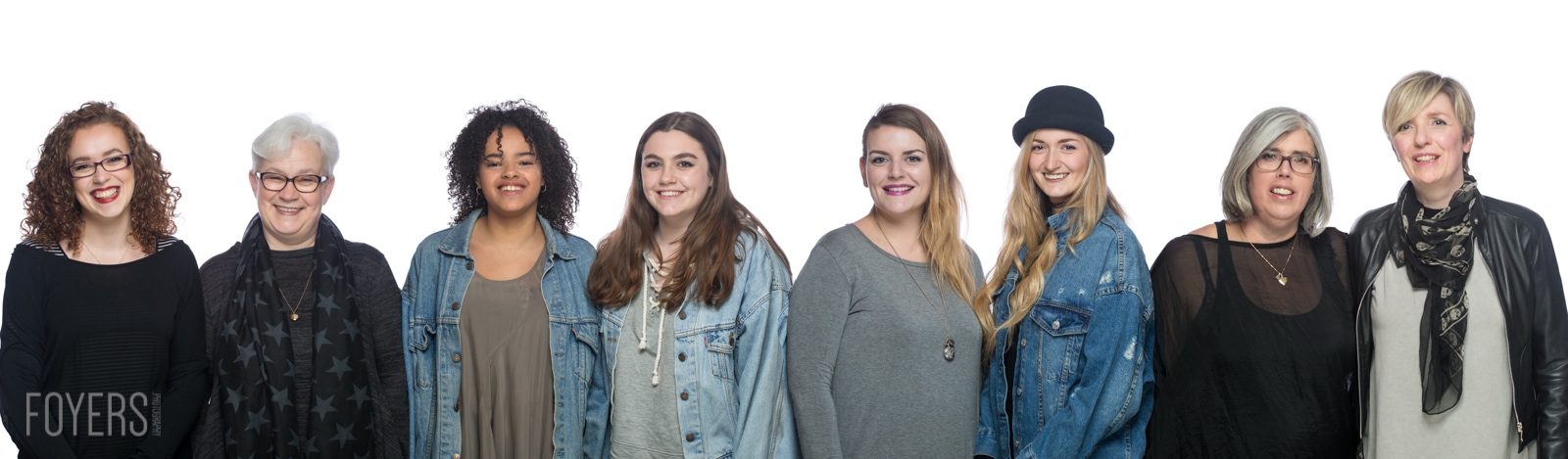 Eight women of varying ages standing in a line against a white background, smiling at the camera. Foyers branding visible.