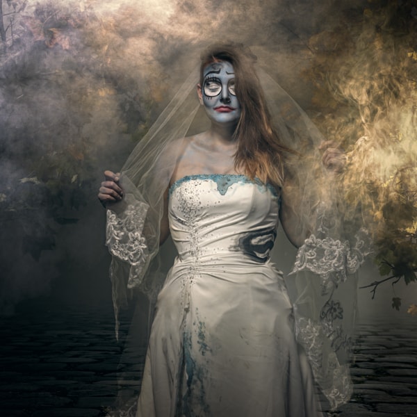 A woman in a white wedding dress and veil with skull face makeup stands in a misty, golden-brown atmospheric setting.