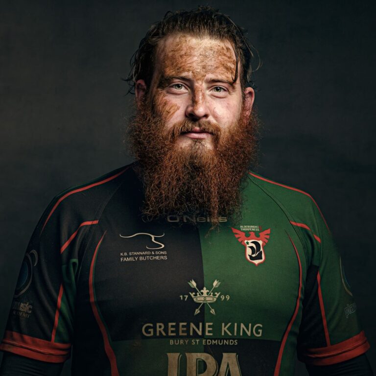 A bearded man wearing a green and black sports jersey with red trim, photographed against a dark grey background.