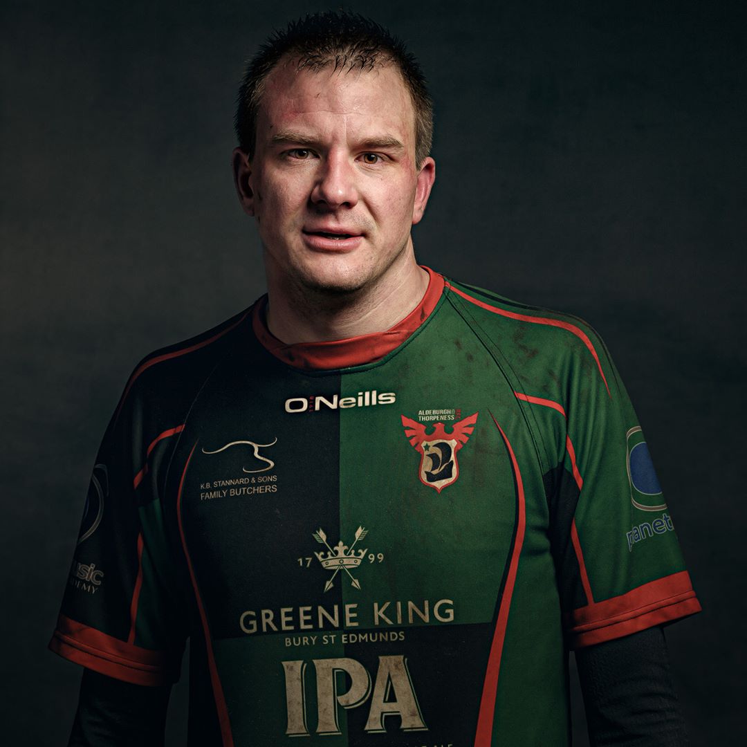 A man wearing a green and black rugby jersey with red trim, photographed against a dark background.