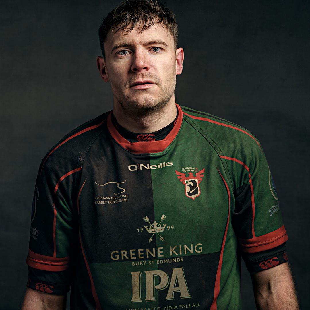 A man wearing a green and black rugby jersey with red trim, photographed against a dark background.