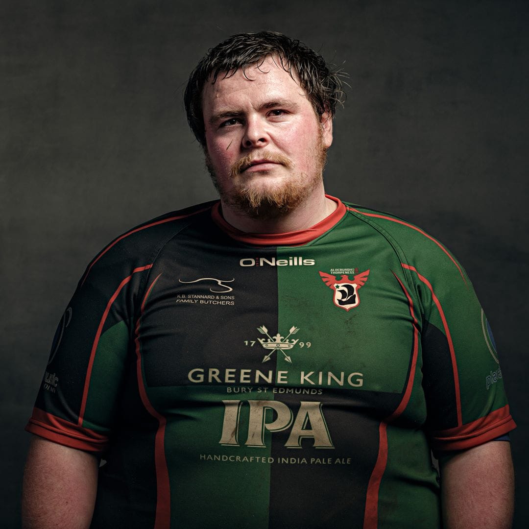 Man wearing a green and black rugby jersey with red trim, photographed against a grey background in a studio portrait.