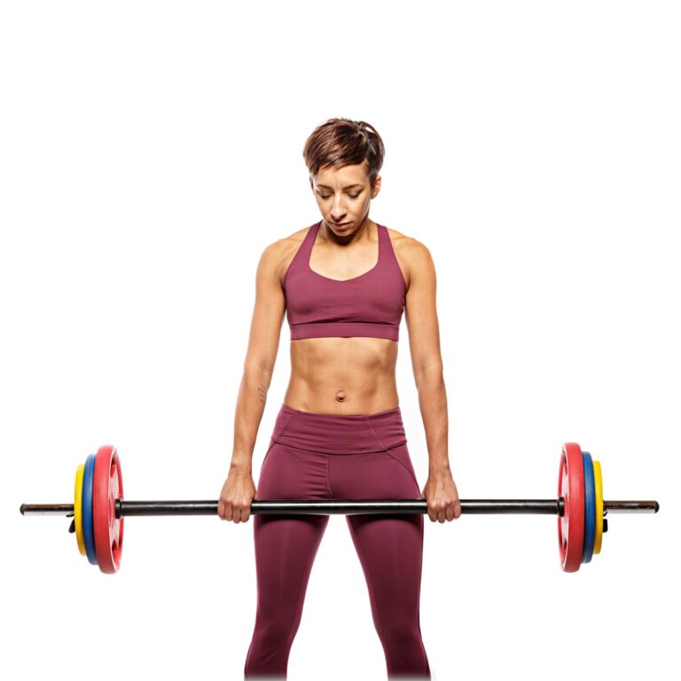 A woman in burgundy sports clothing holds a barbell with red, blue and yellow weight plates against a white background.